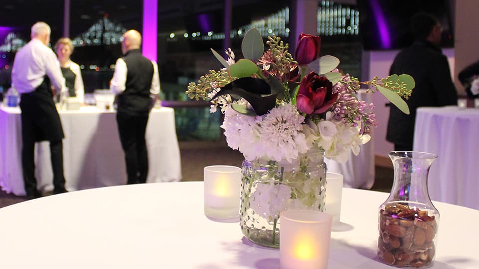 Vase of flowers and candles on a table. A few people in the distance. 