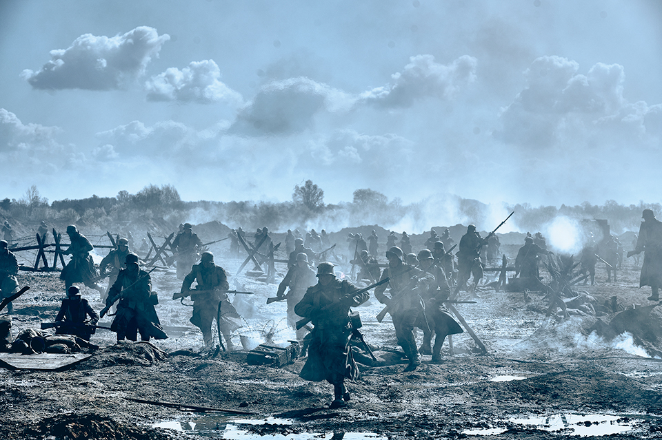 A war scene. Soldiers are seen running and carrying guns. The ground is muddy. The image is grey and dark, but the sky is quite light. Still taken from Netflix film All Quiet on the Western Front. Copyright - ReinerBajo - Netflix.
