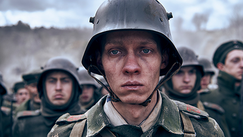 A soldier's face, head and shoulders. He looks into the distance. He is wearing uniform and a helmet. In the background there are other soldiers. Still taken from Netflix film All Quiet on the Western Front. Copyright - ReinerBajo - Netflix.