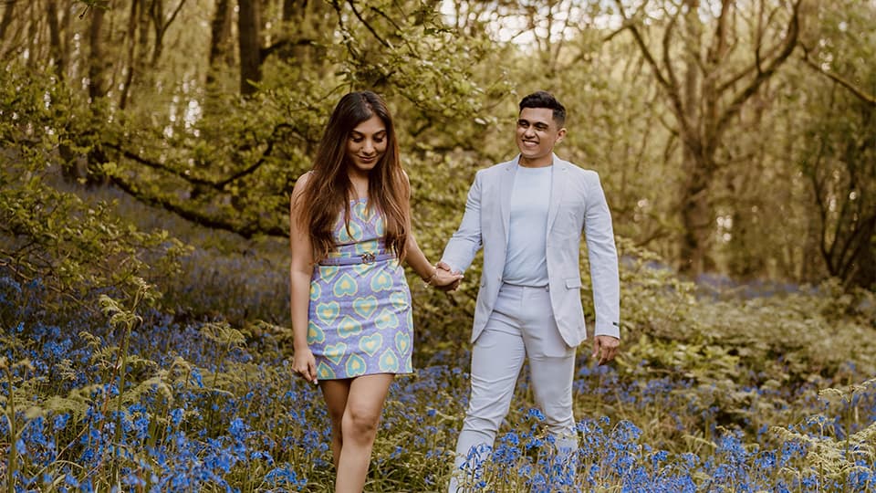 Aditya Mukherjee and Aarushi Mittal walking through the bluebells at Burleigh Wood, Loughborough University. They are walking holding hands and smiling together.