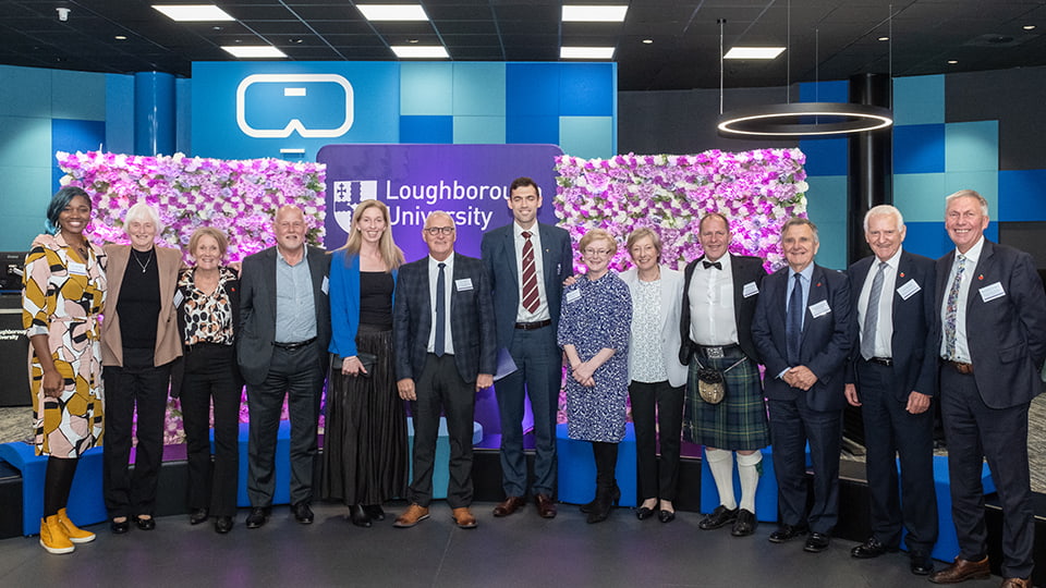A group of Hall of Fame members standing together in front of a Loughborough University banner and flower walls.