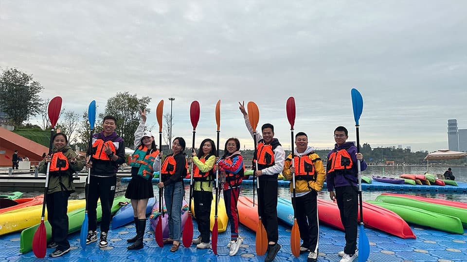 A group of nine alumni in Chengdu at a holding paddles and smiling together at the alumni gathering on 26th October near a lake.