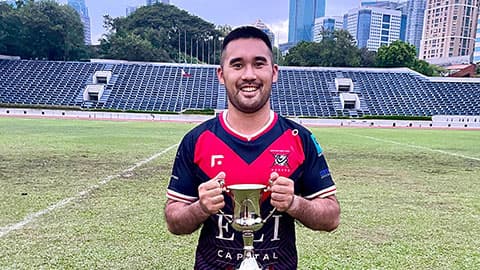 Callum holding the Presidents Cup on a rugby pitch. He is grinning and standing their in his rugby kit.