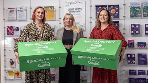 Three people standing. Two of them are holding green boxes.