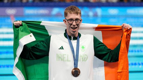Daniel Wiffen poses with his gold medal wearing an Ireland tracksuit top and holding a flag