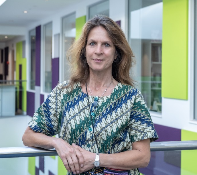 Professor Eef Hogervost wearing a green patterened dress and stood in front of an office space that is purple and green colour schemed.