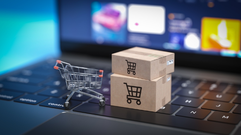 A laptop with a small supermarket trolley sat on the keys and two small cardboard boxes with images of trolleys on them