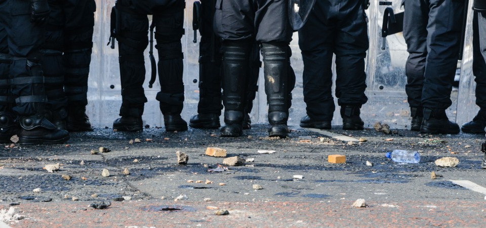 a line of police stand in debris thrown during a riot