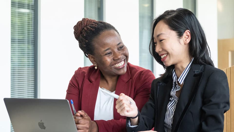 Two students dressed smartly, sitting at a table with a laptop, having a discussion.