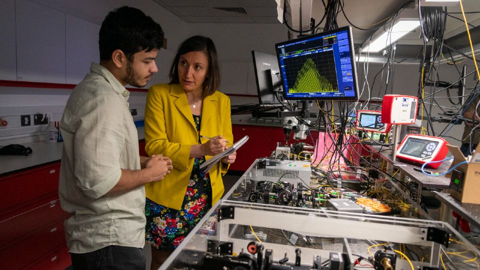 A man and a woman stood over photonics research equipment in conversation