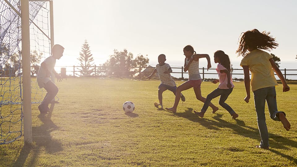 3 children playing footback with sun shining in background