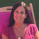 Cath, sitting on a chair, smiling, looking directly at the camera