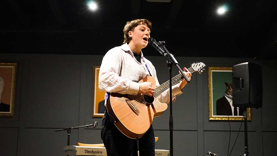 A performer singing and playing a guitar on stage.