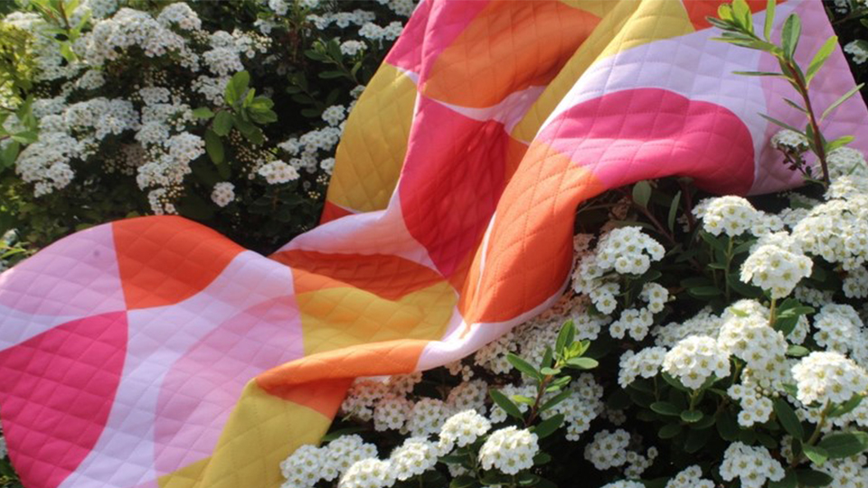 Photo of one of the play orange and pink patchwork playmats Ella created on a bed of flowers