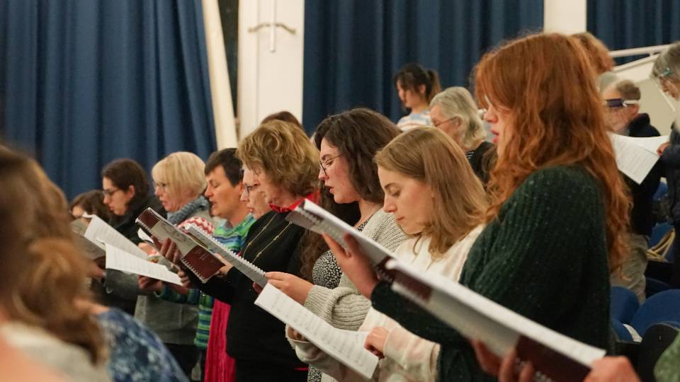 Group of people singing whilst reading from songbooks.