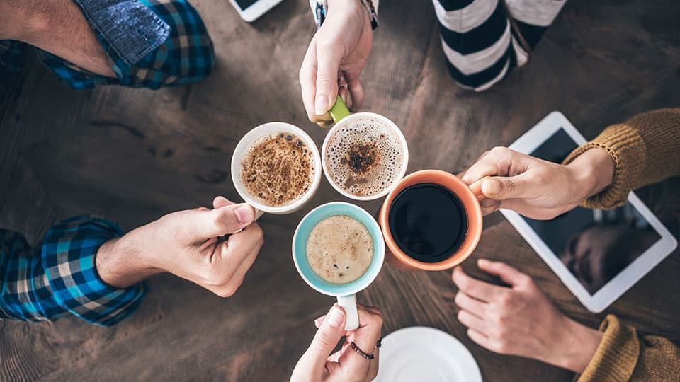 An aerial view of four people's hands holding mugs of tea/coffee in a circle. 