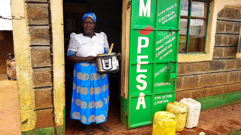 Photo of a woman stood in doorway of building with a cooker in her arms