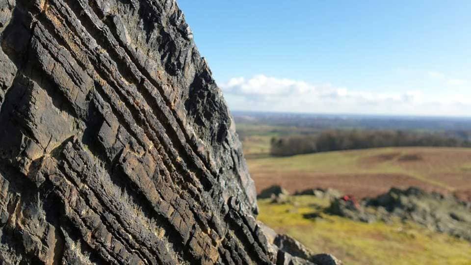 A textured rock with blue skies and fields of grass in the background.