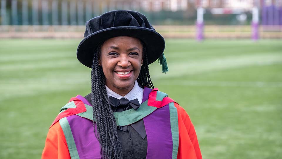 Diane wearing graduation wear smiling at the camera stood outside on a playing field