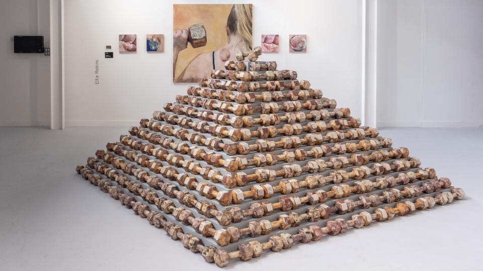 A pyramid of ceramic dumbbells and a display of paintings in a gallery.