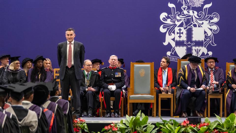 Steve stood on the graduation stage wearing a suit and looking out to the crowd