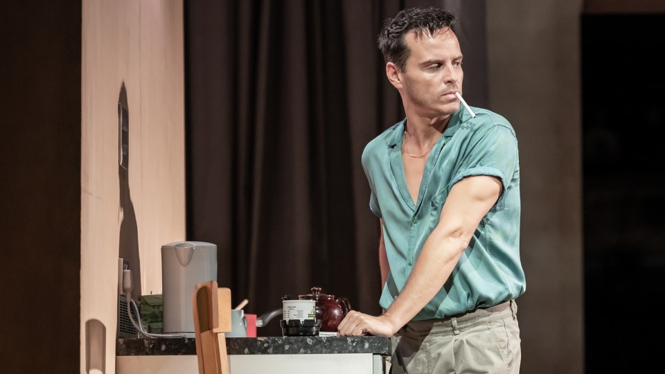 Andrew Scott on stage during a production of 'Vanya', he is leaning on a kitchen counter with a cigarette in his mouth and is looking over his shoulder.