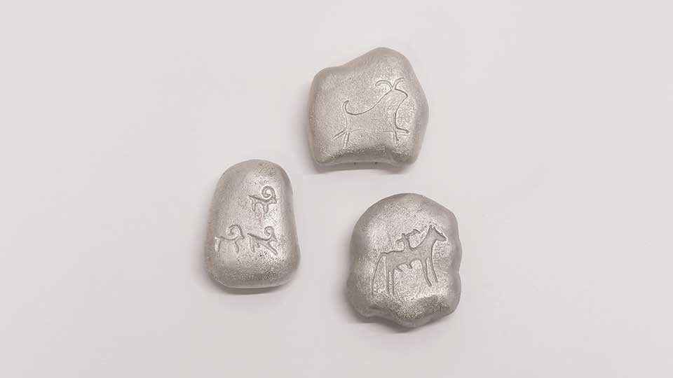 Three silver pebble-sized brooches of abstract shape engraved with simple animal drawings.