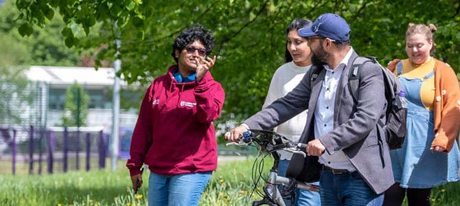 three students walking together one wheeling a bike. two students chatting behind the three