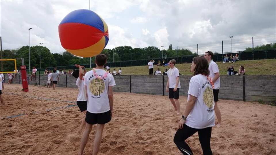 A group of people playing volleyball on a sandy beach, with a ball floating inthe air.