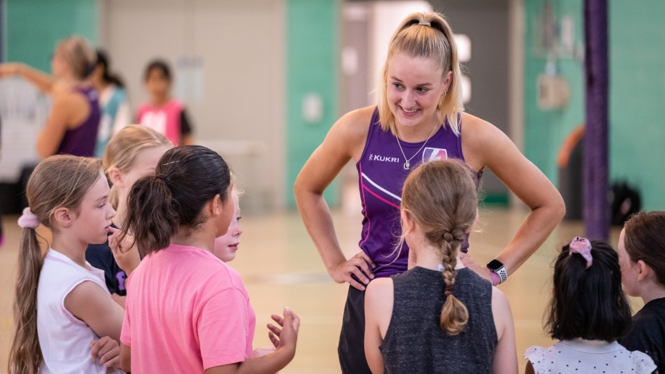 A netballer teaching young girls