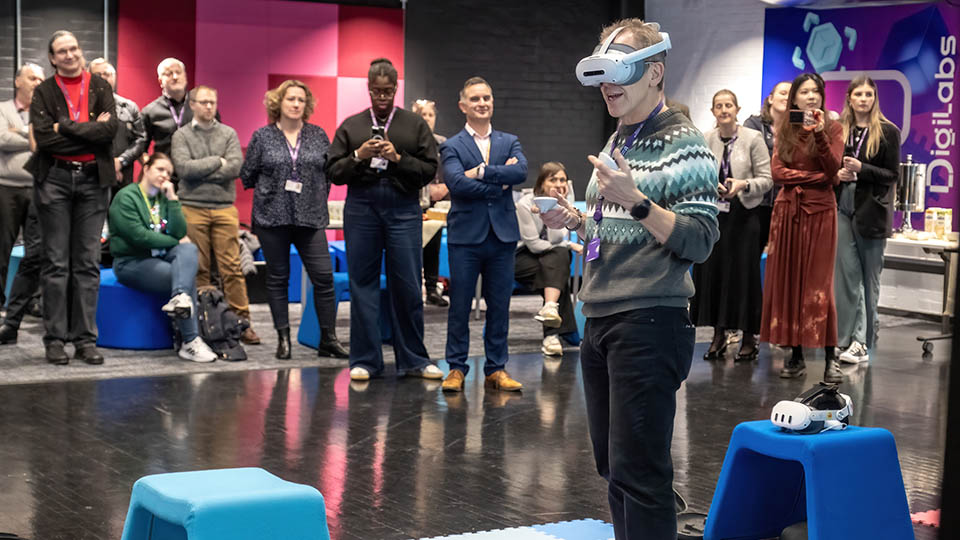 A man stood wearing a VR headset in front of a group of staff and students inside one of the DigiLabs