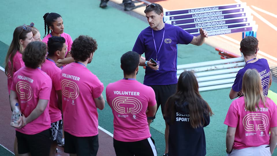 A group of people wearing volunteer t-shirts standing together on an athletics pitch.