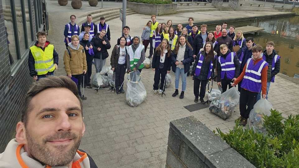 A group of Loughborough staff and students standing outdoors holding bags of lrubbish and litter picker tools.